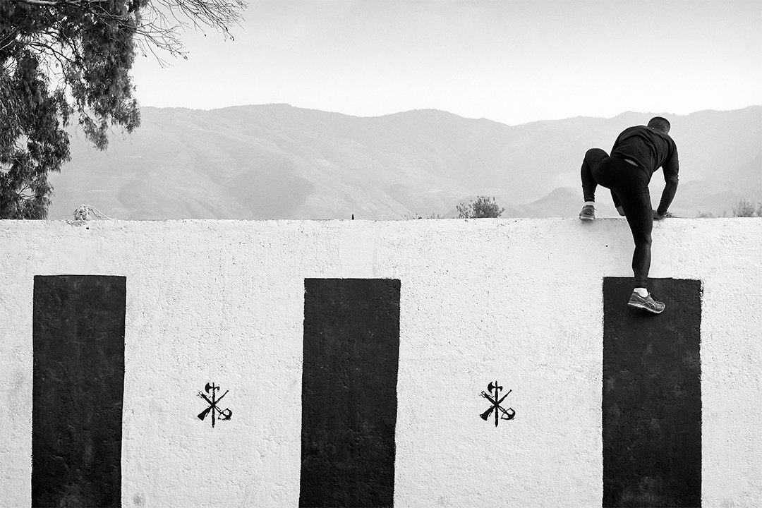 A service member climbing over a wall on an obstacle course.